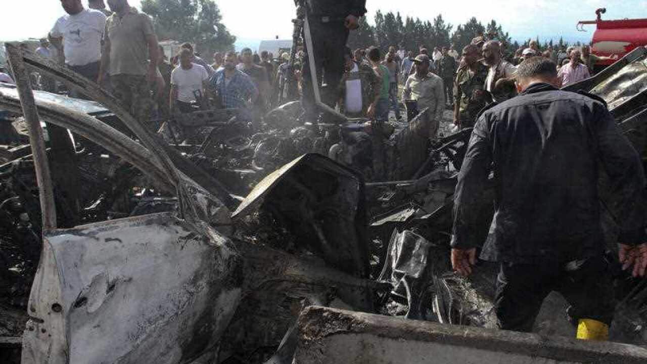 In this photo released by the Syrian official news agency SANA, Syrian security forces, emergency services and residents look at the remains of burned vehicles