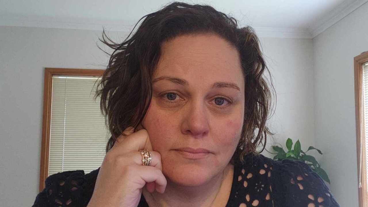 A woman with short brown hair with her hand held up to her cheek