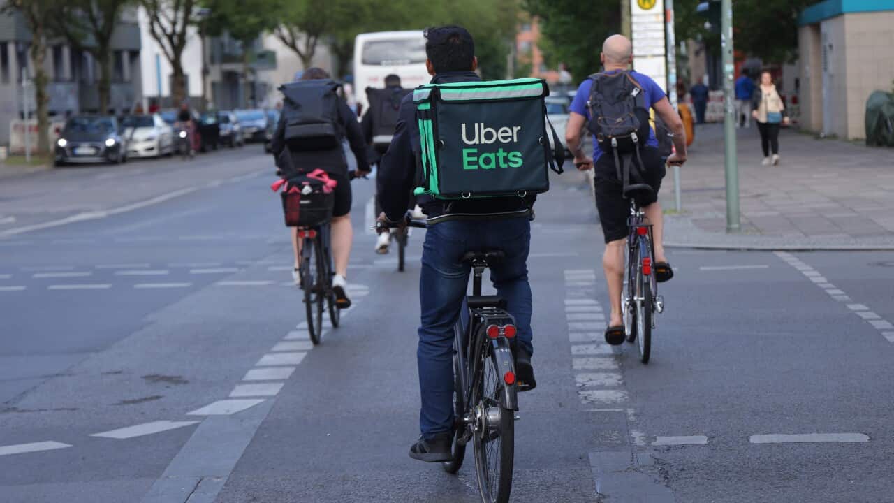 An Uber Eats food courier rides a bike across an intersection with several other riders.