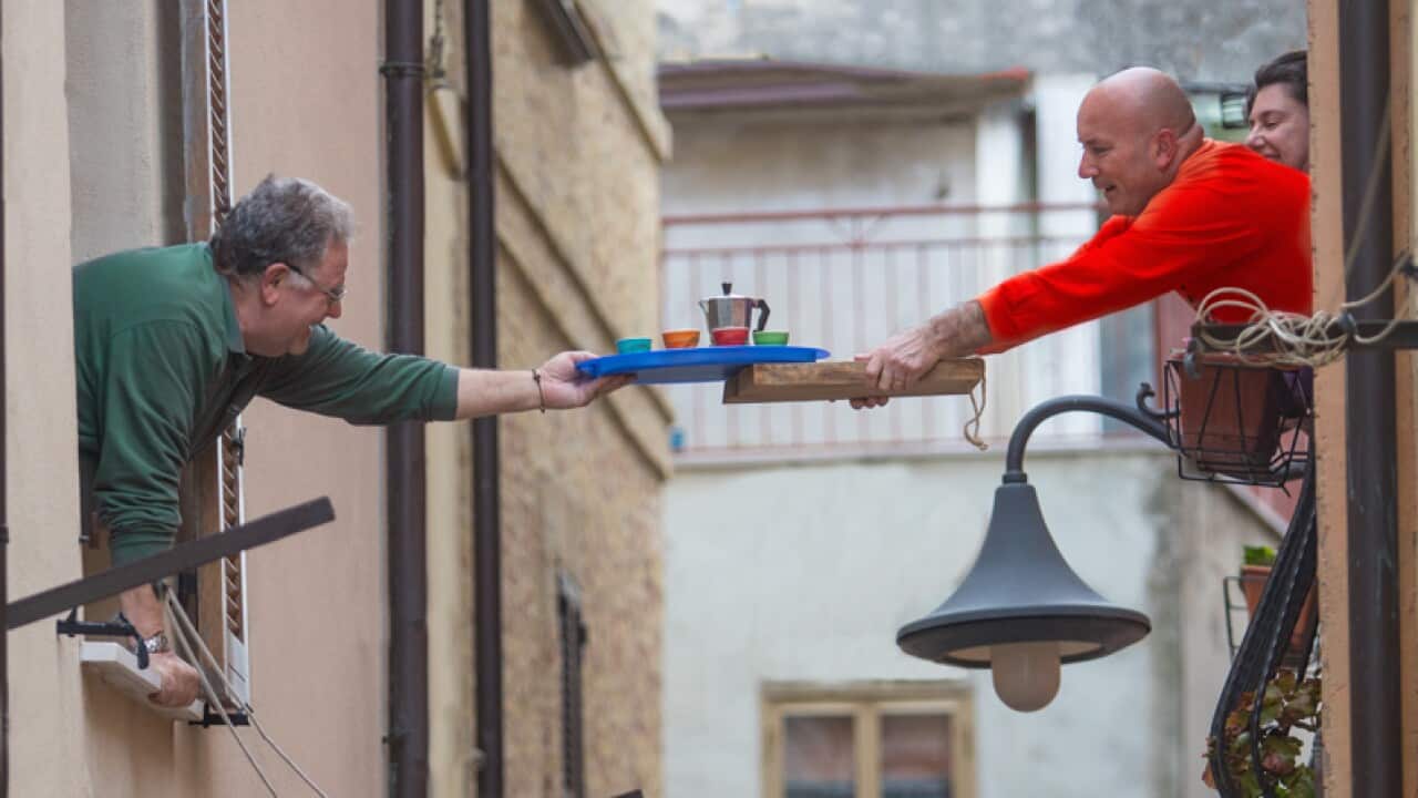 Two neighbours pass a tray with coffee from one window to the other