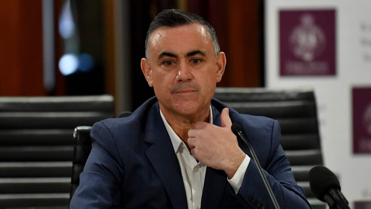 A white man in a blue suit sits at a table in front of a microphone