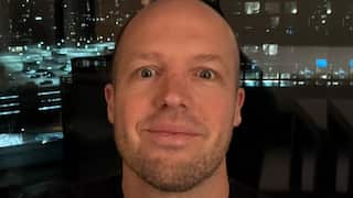a close up of a middle aged bald man in front of a city landscape at nighttime