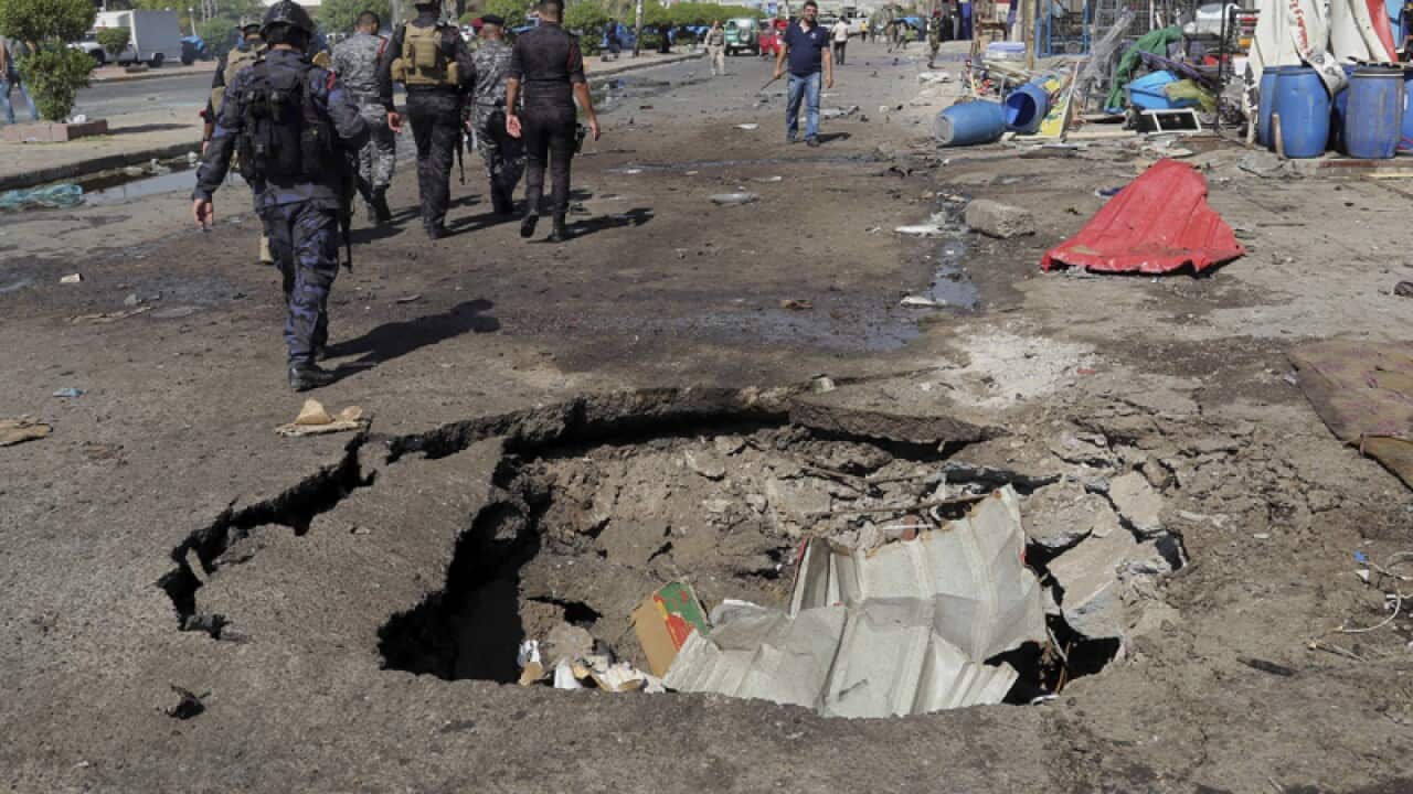 Security forces walk past a crater caused by a car bomb explosion