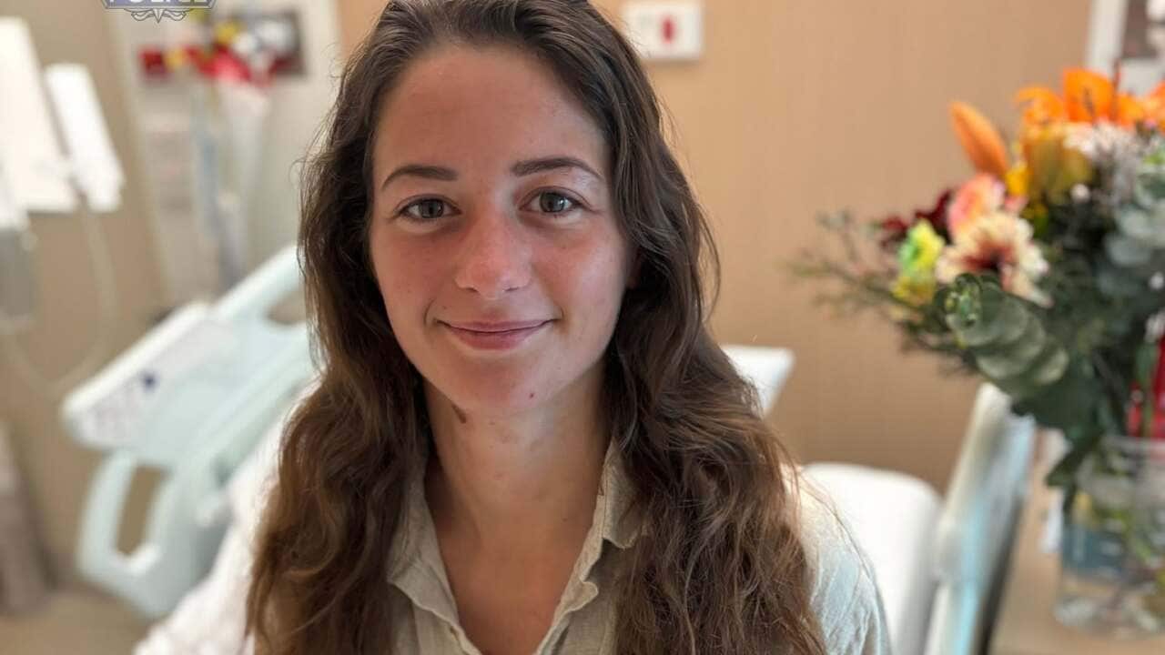 Carolina Wilga sitting in a hospital bed, holding a teddy bear.