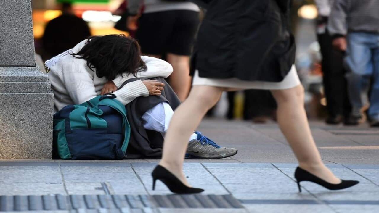 A homeless woman sits on a street corner