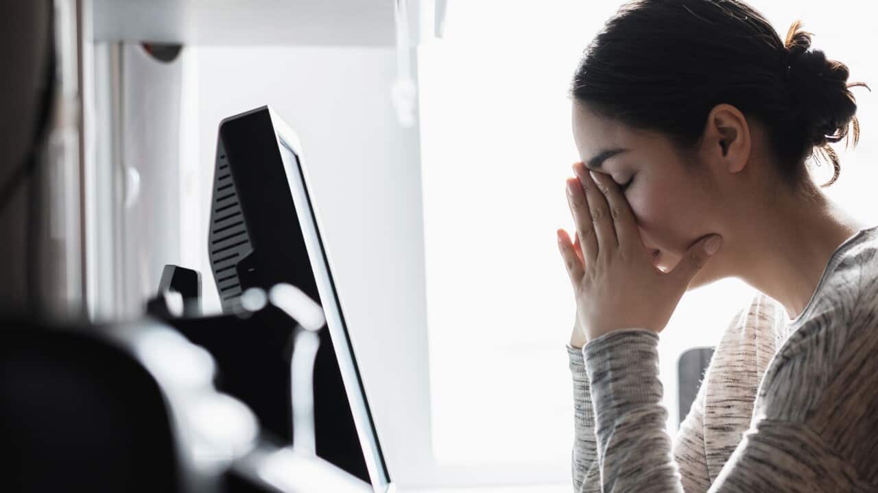 A woman resting her face on her hands while seated in front of a computer.