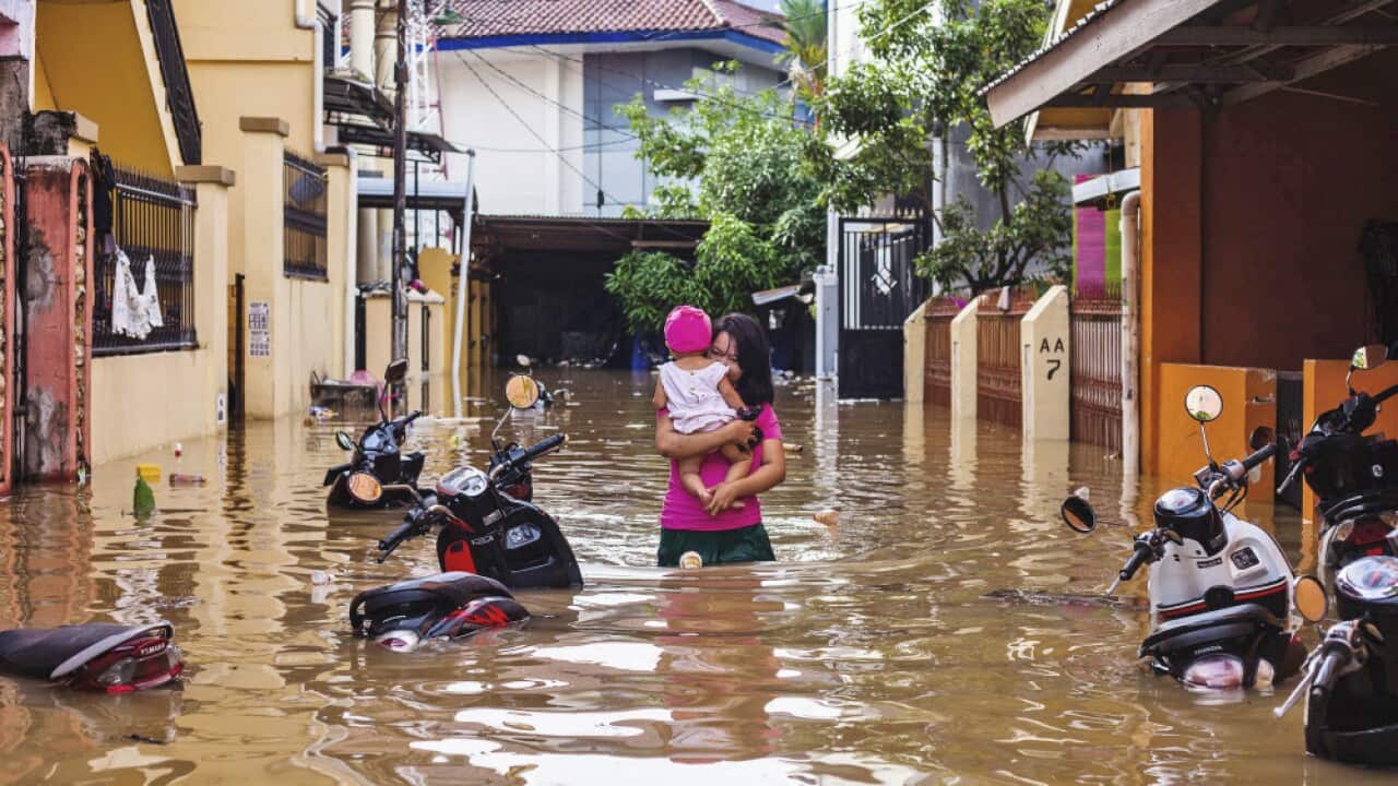 A woman carries her daughter as she wades through a flooded neighborhood in Makassar, South Sulawesi, Indonesia,