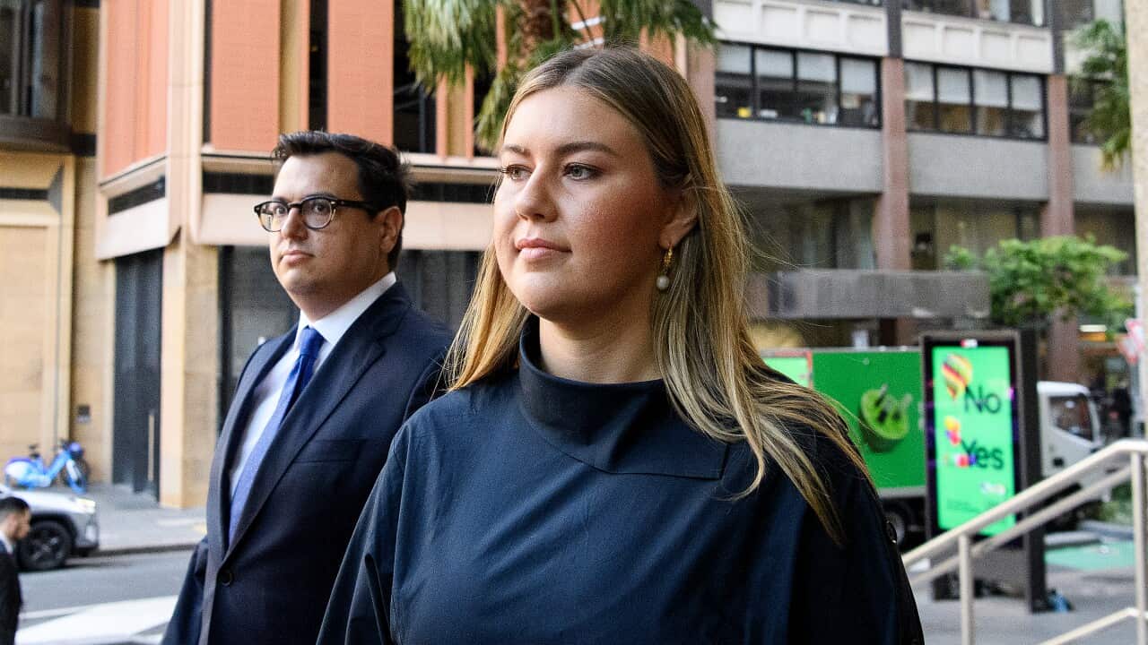 Brittany Higgins, wearing a navy blue dress, arrives at the Federal Court of Australia flanked by her partner David Sharaz, who is wearing a suit.