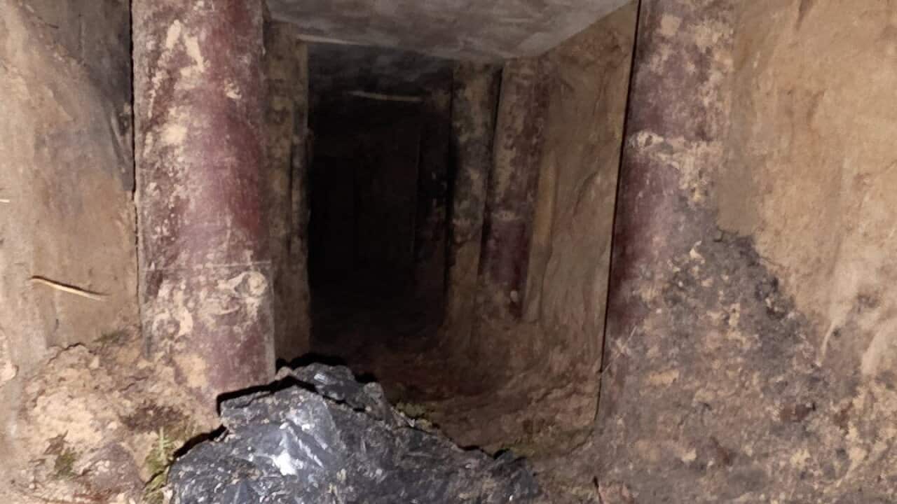 A dark underground tunnel with wooden supports holding up a low cieling.