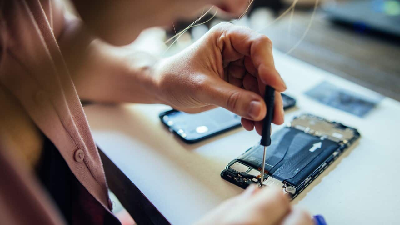 Woman repairing mobile phone at home, changing damaged part.