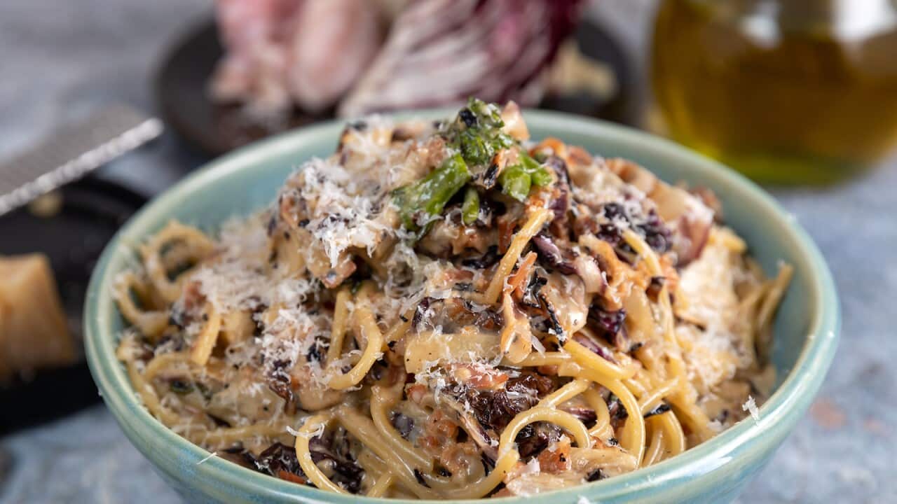 A blue pottery bowl is filled with pile of spaghetti in a light creamy sauce, with brown pieces studded through the sauce.