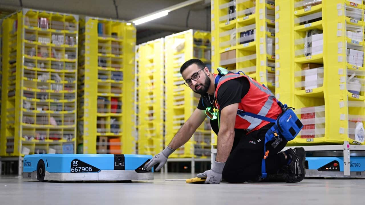 Amazon floor manager, Reza Faqiri, poses with an Amazon robot at a Sydney fulfilment centre in 2023