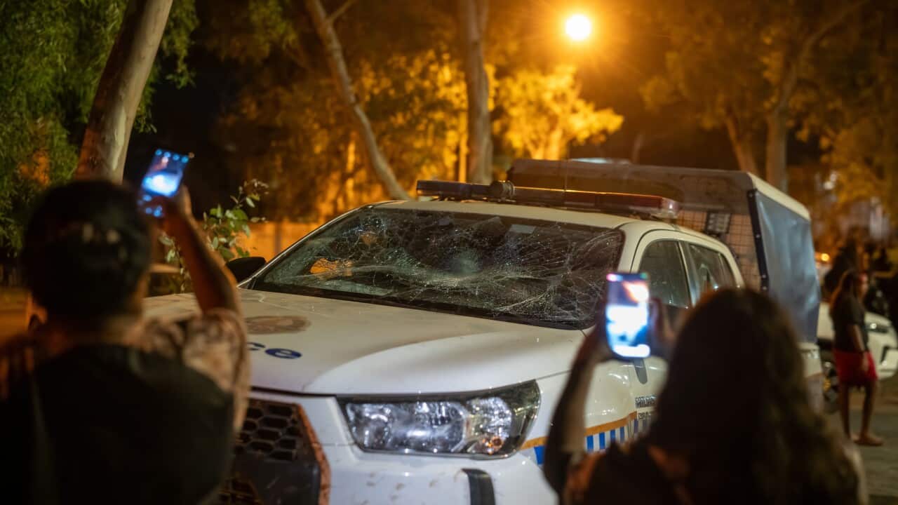 Two people hold up their smartphones to take photos of a damaged police vehicle