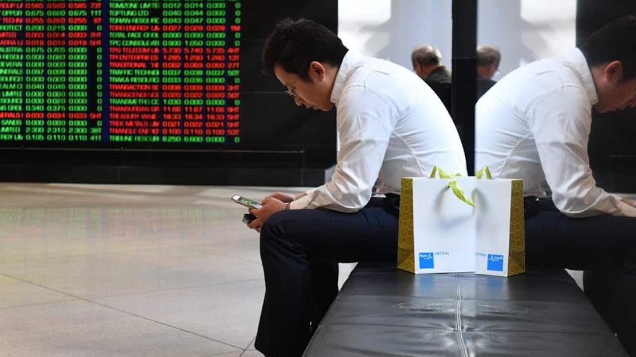 A man looks at his phone in front of the ASX board.