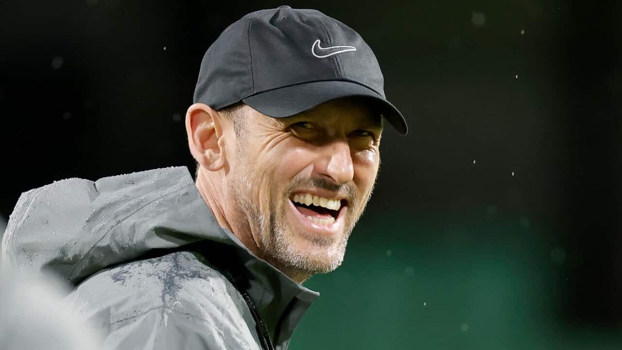 A man wearing a black jacket and cap and smiling