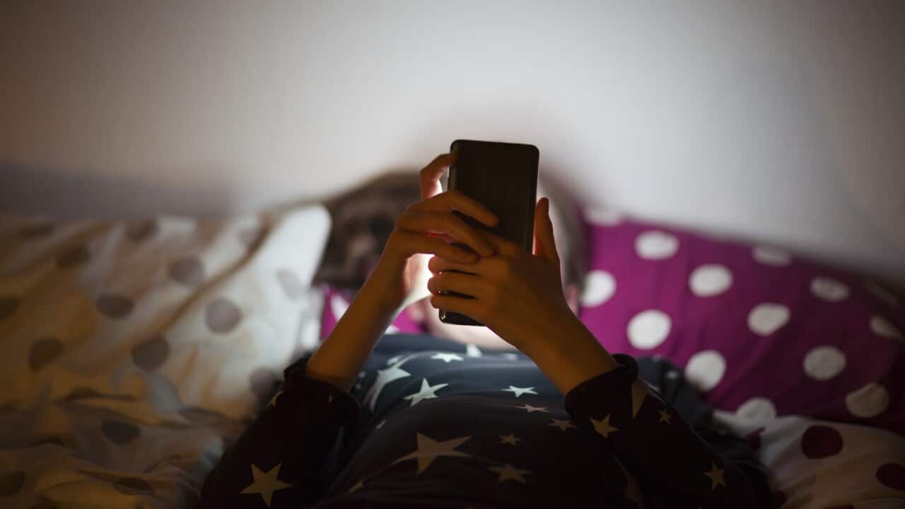 A girl lying on bed at night and using a mobile phone.