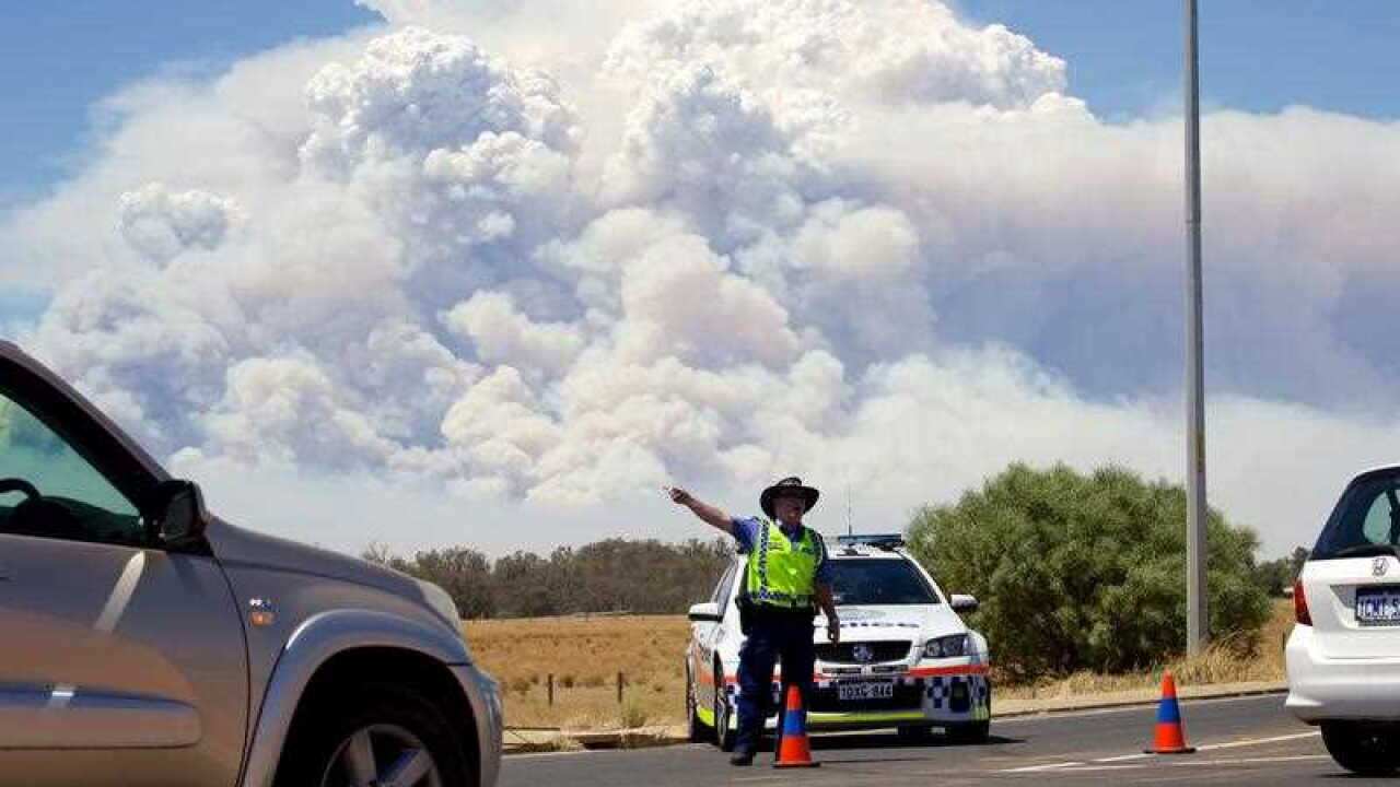 Smoke clouds from a large bush fire are seen behind a police road block at the turn off onto the South Western Highway near Pinjarra, Western Australia.