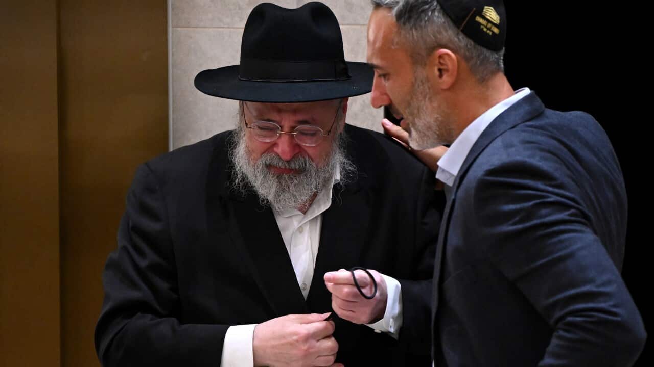Man wearing a black hat being consoled by a man wearing a kippah.