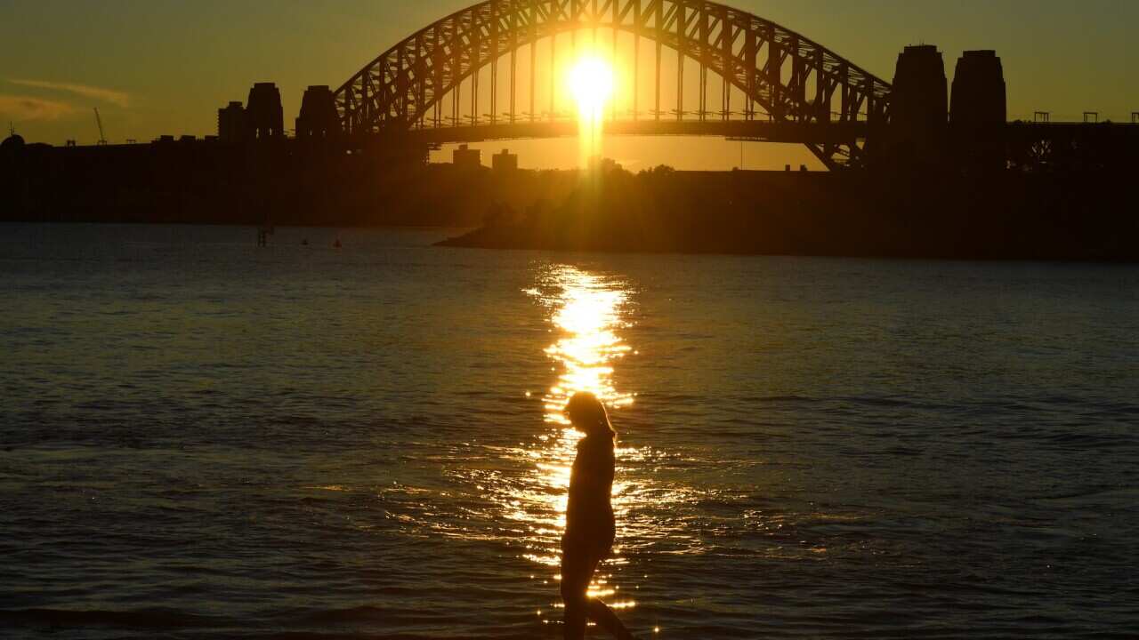 A woman walks past the Sydney Harbour Bridge at dawn in Sydney.