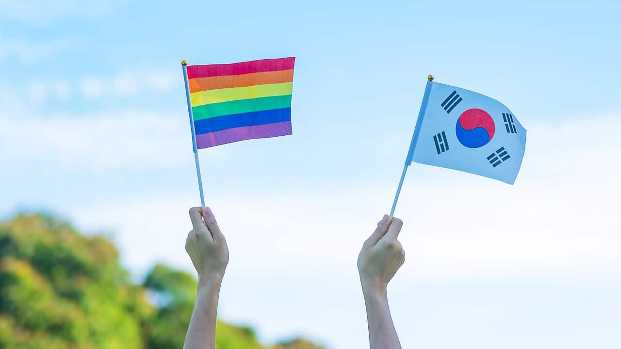 Two hands holding an LGBTIQ+ rainbow flag and a South Korea flag.