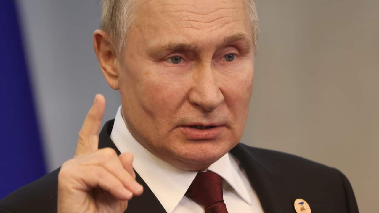 A man wearing a suit and tie speaks in front of a microphone.