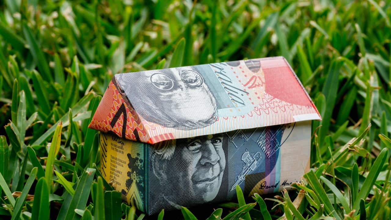 An origami house made out of Australian money sitting on grass.