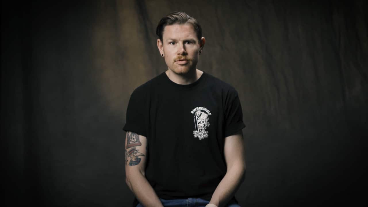 A man in a black t-shirt with tattoos sitting.
