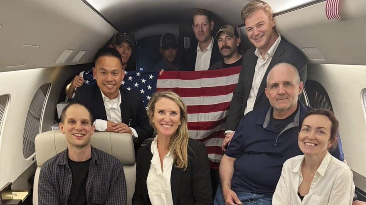Several people post for a photo inside what appears to be a plane. One is holding a US flag.