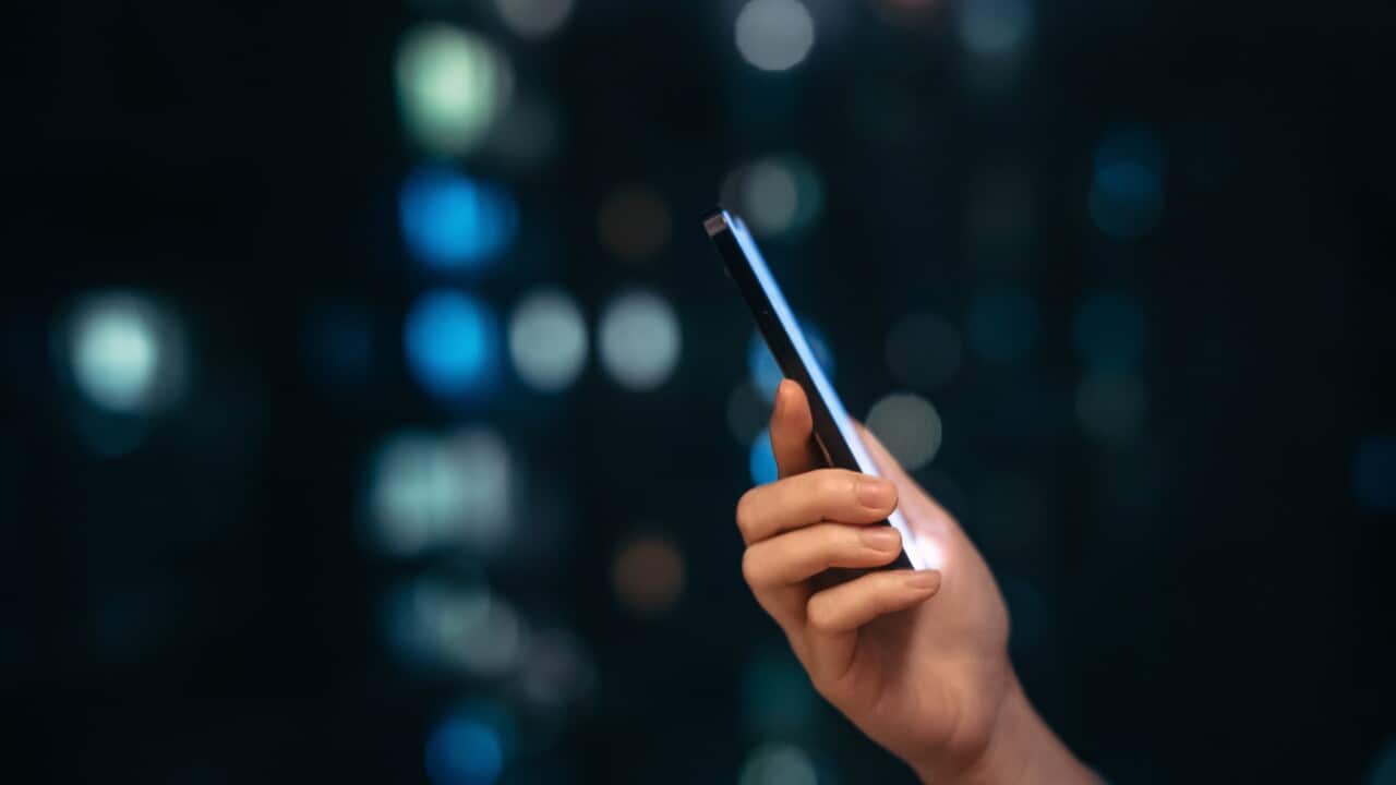 Close up shot of female hand using smartphone at night, against illuminated and defocused bokeh in background. Lifestyle and technology