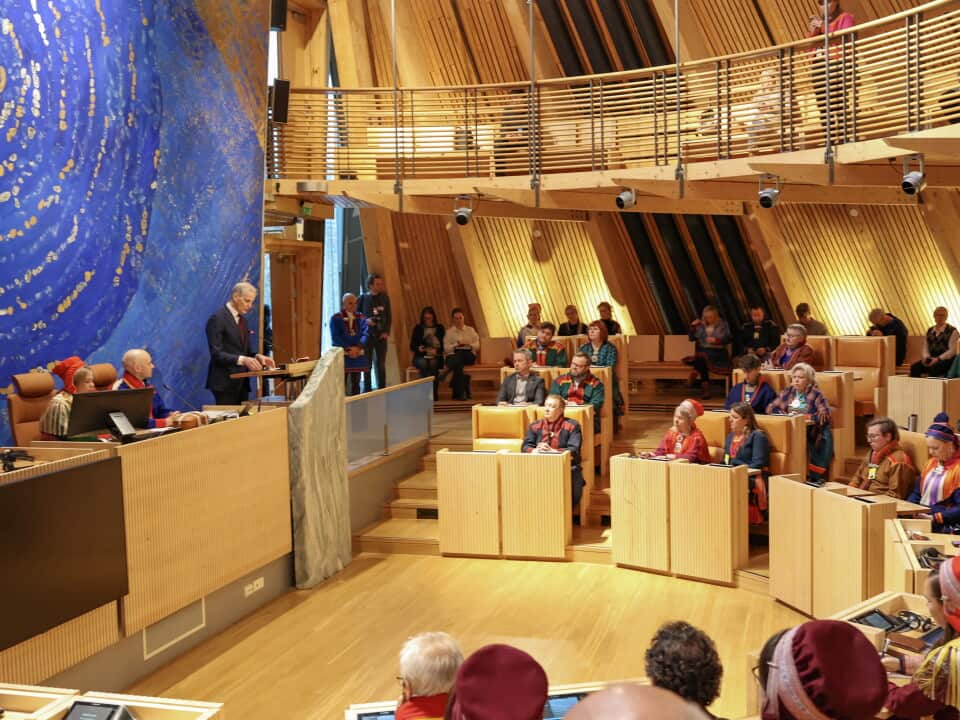 Delegates seated in a semi-circle- facing a speaker in the Sami Parliament building.