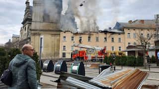 A man in Ukraine stands in front of a military drone as a building burns in the background
