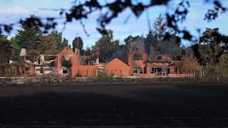 A burned-out red-brick house in front of a blackened field.