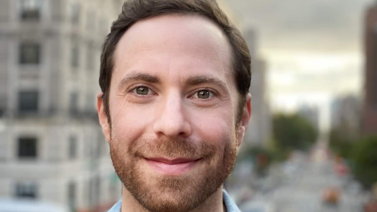 A portrait shot of a man in a blue shirt smiling at the camera.