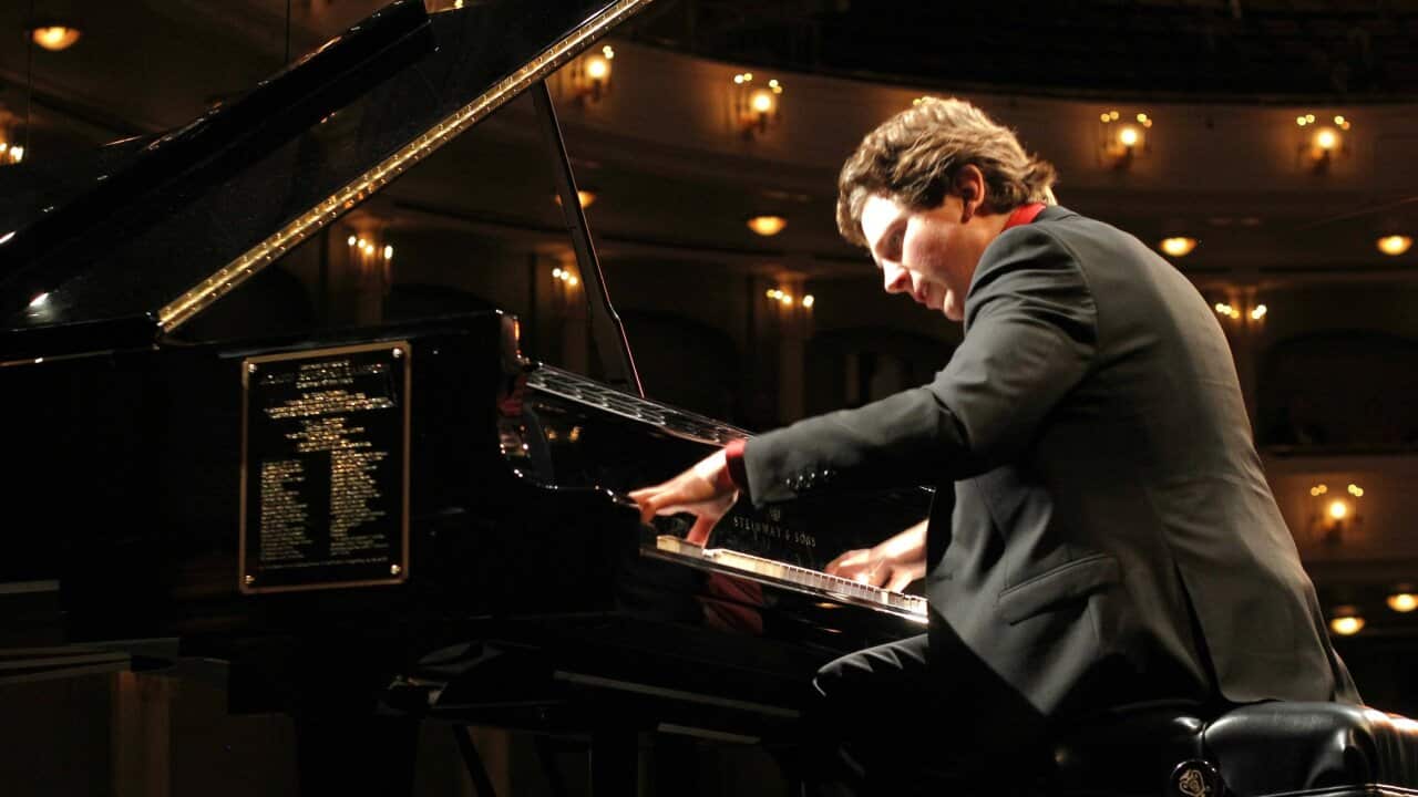 Jayson Gillham dressed in a suit, playing the piano.