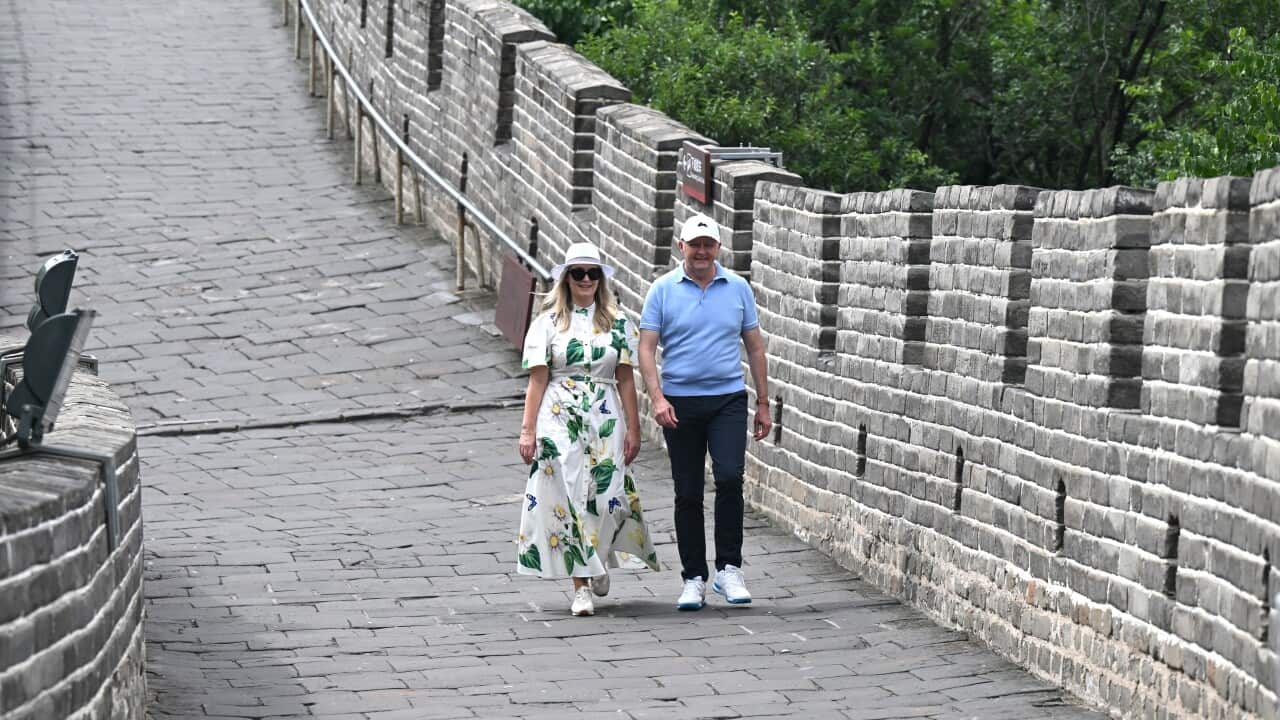 A man in a blue polo and a woman in a white and green floral dress walk along the Great Wall of China.