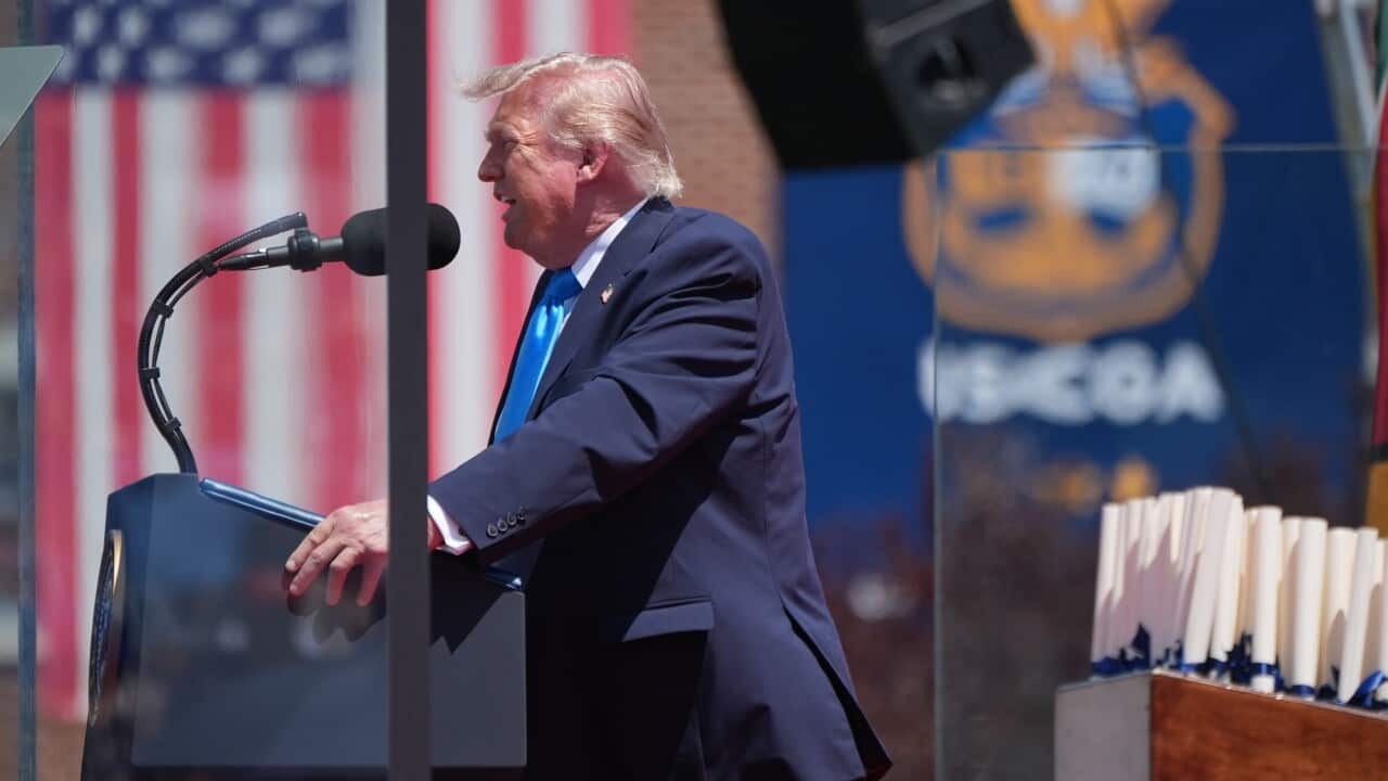 A man wearing a navy blue suit and a blue tie speaks at a podium