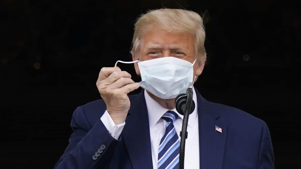President Donald Trump removes his face mask to speak from the Blue Room Balcony of the White House to a crowd of supporters.
