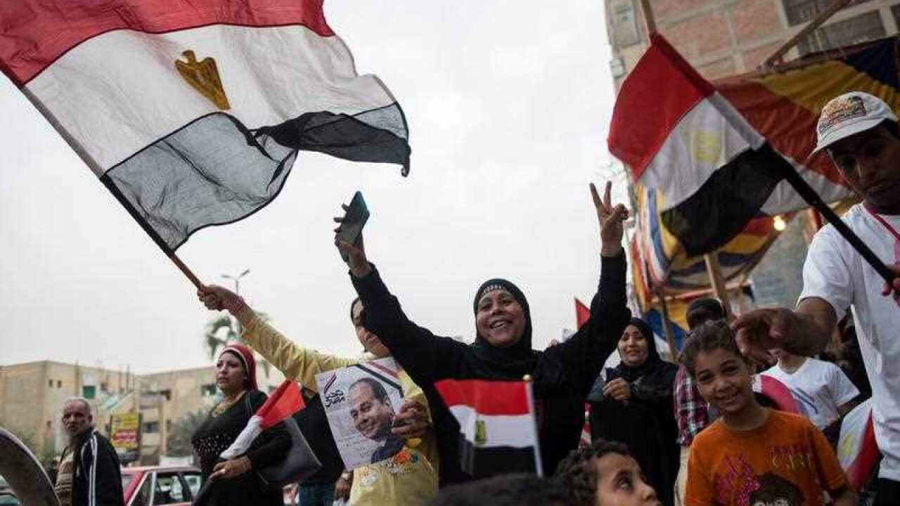 People hold a photo of President Abdel Fattah al-Sisi, and wave national flags on the final day of the Egyptian presidential election