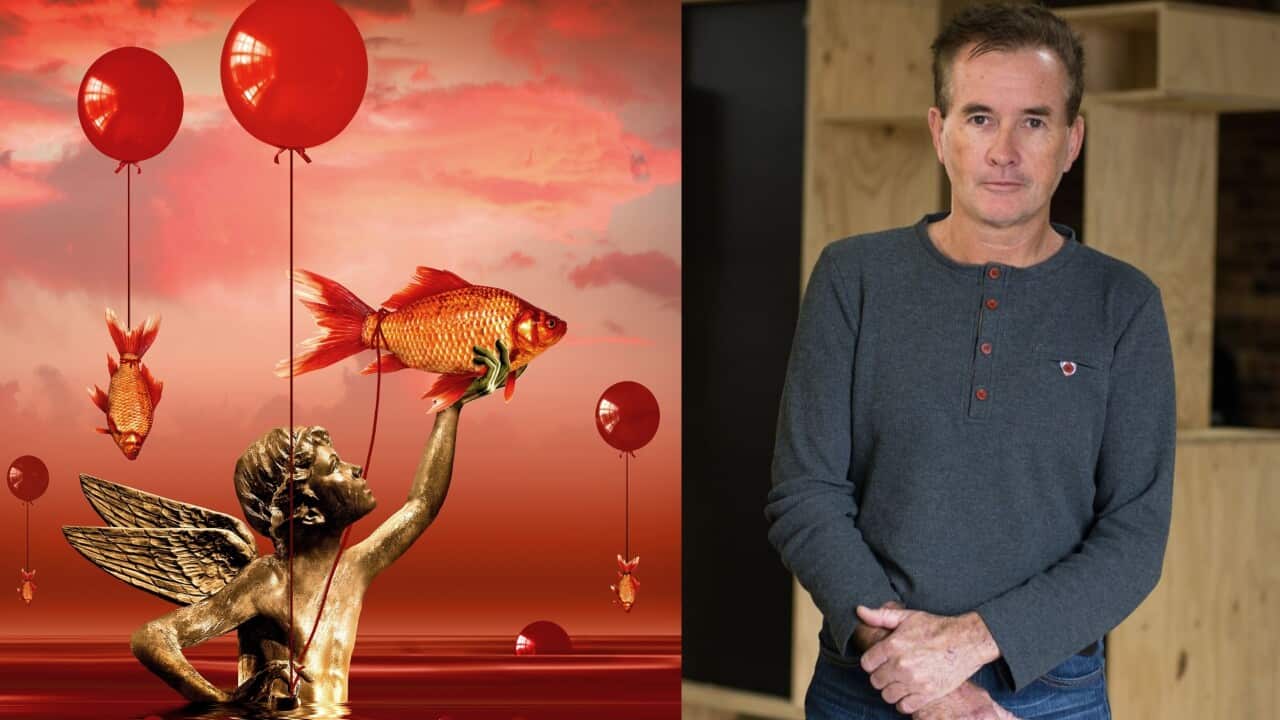 Artwork featuring a gold statue of a boy with wings holding up a goldfish with his left hand. The fish has a red cord around its tail. Another fish with a red cord around its tail is suspended.