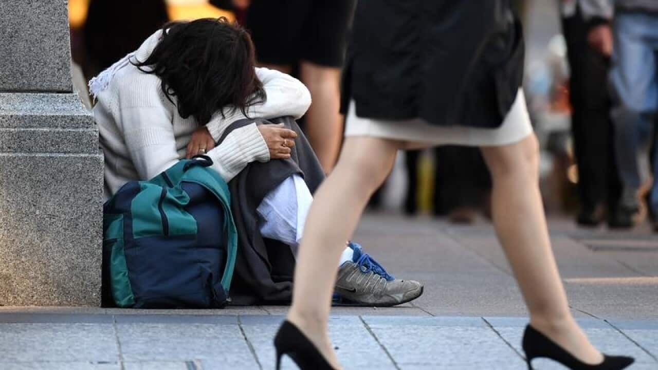 A homeless woman sits on a street corner.