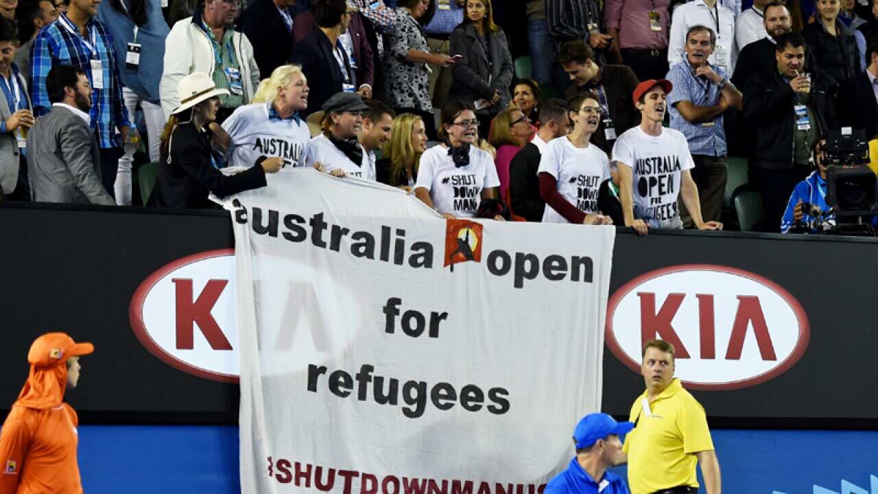 A refugee activist holding signs saying "Australia Open for Refugees"