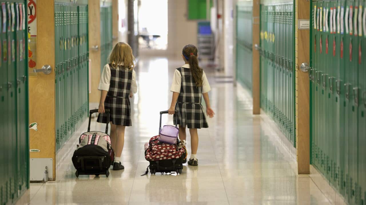 Two students roll their backpacks in a school.