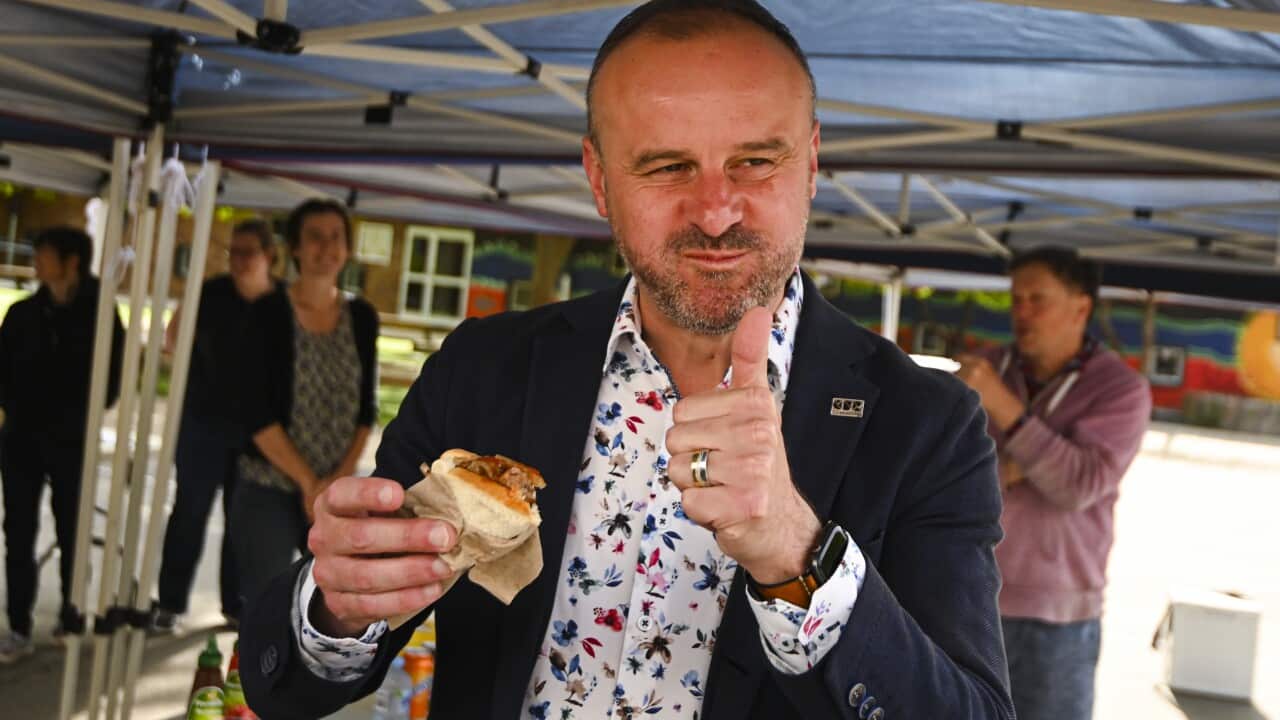 Chief Minister of the ACT Andrew Barr reacts after taking a bite from a democracy sausage as he visits a polling booth.