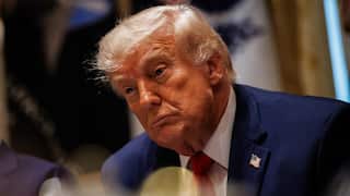 US President Donald Trump, wearing a suit and tie, listens during a meeting.