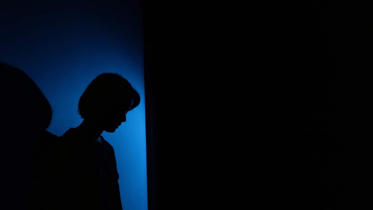 A silhoeutte of a woman against a wall, with blue light peering through.