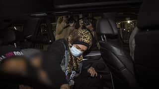 A woman wearing a headscarf and facemask gets into a car while members of the media take her photo.