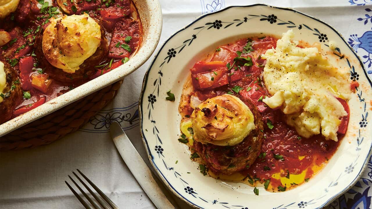 A serve of oven-baked meatballs and mash sits on a plate on a cloth with floral blue edging.