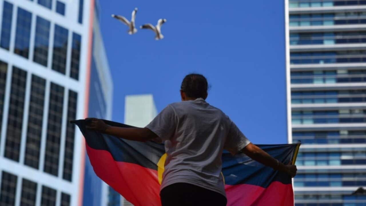 A protester holds an Aboriginal flag at the Black Deaths in Custody Rally at Town Hall in Sydney, Saturday, April 10, 2021.