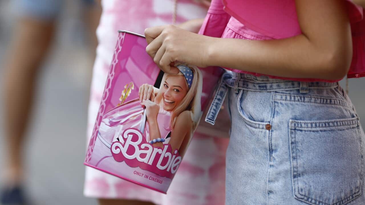 A person holding a popcorn box with the image of Margot Robbie as Barbie.