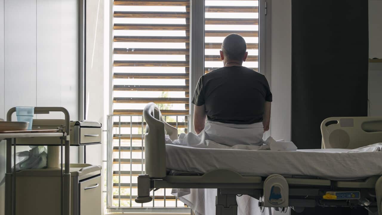 Man sitting on a hospital bed facing away from camera.